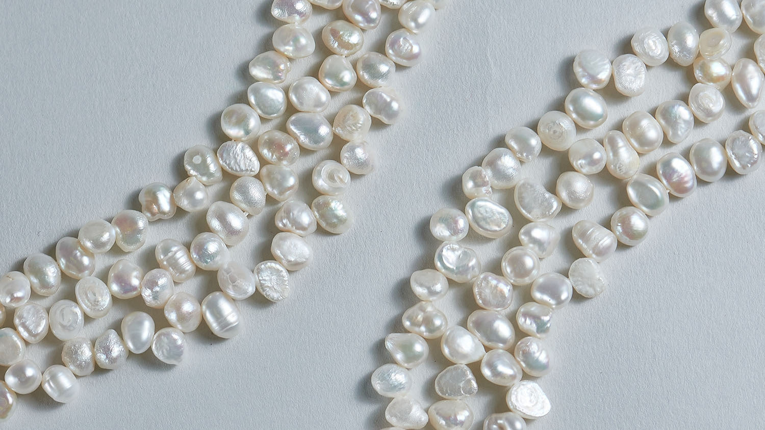 The image shows two rows of loose baroque freshwater pearls with grey background.
